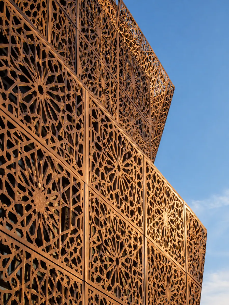 Primer plano de una fachada de celosía ornamental color bronce que brilla bajo el sol de la tarde